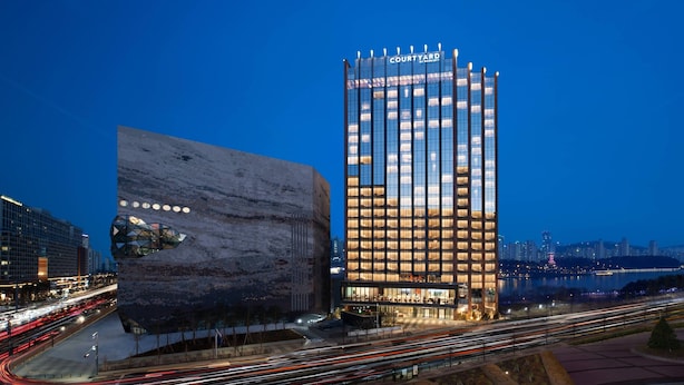Un hôtel moderne à l’architecture originale, avec une façade rappelant la roche et un bâtiment imposant doté d’une façade en verre et de fenêtres illuminées.