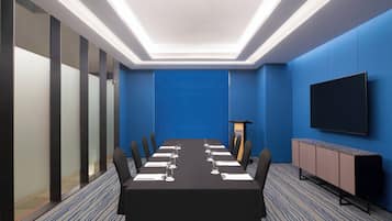 A conference room with a long table, chairs, a podium, and a TV on the wall.