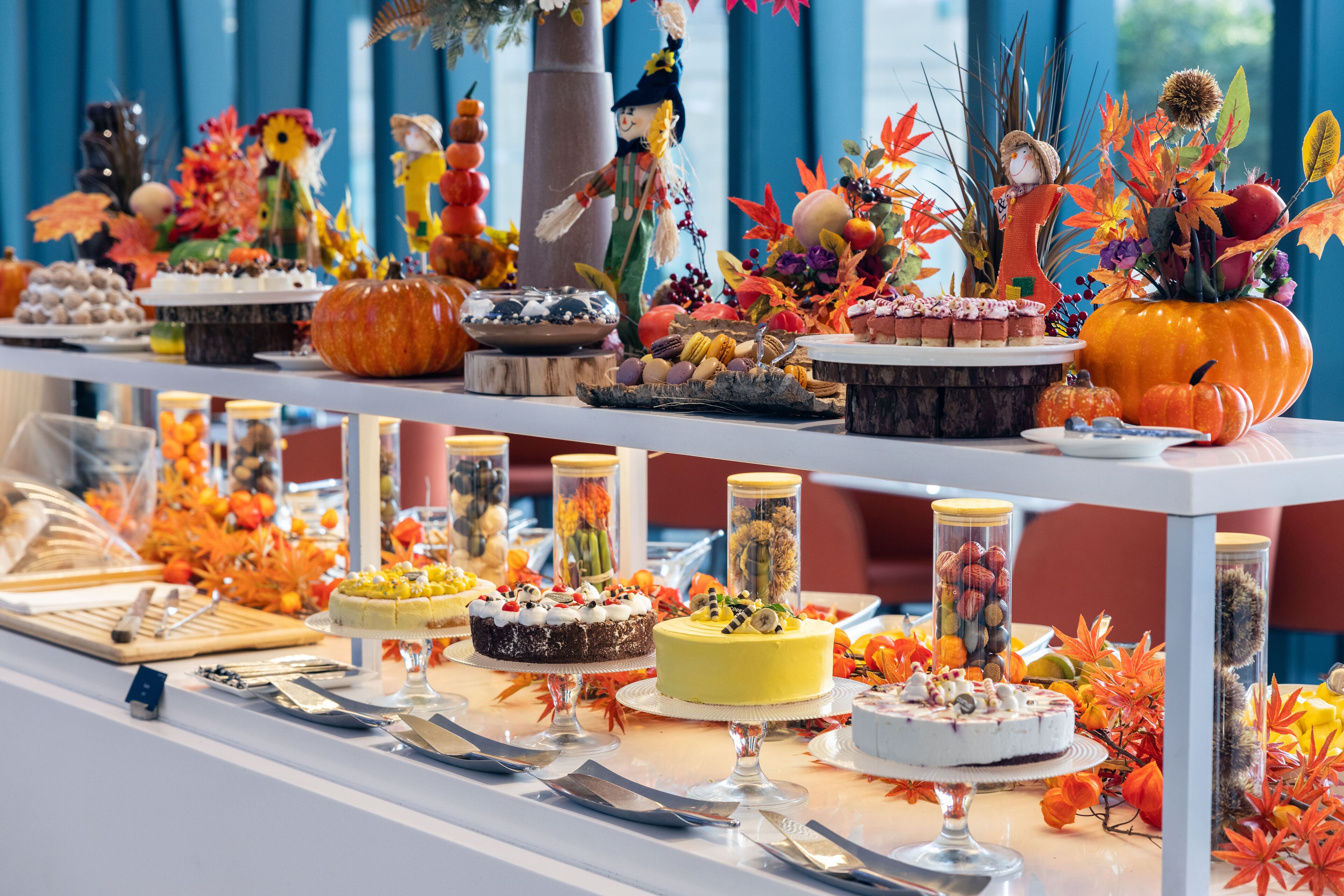 Una mesa de bufé con diversos postres y adornos, incluyendo calabazas y hojas de otoño.