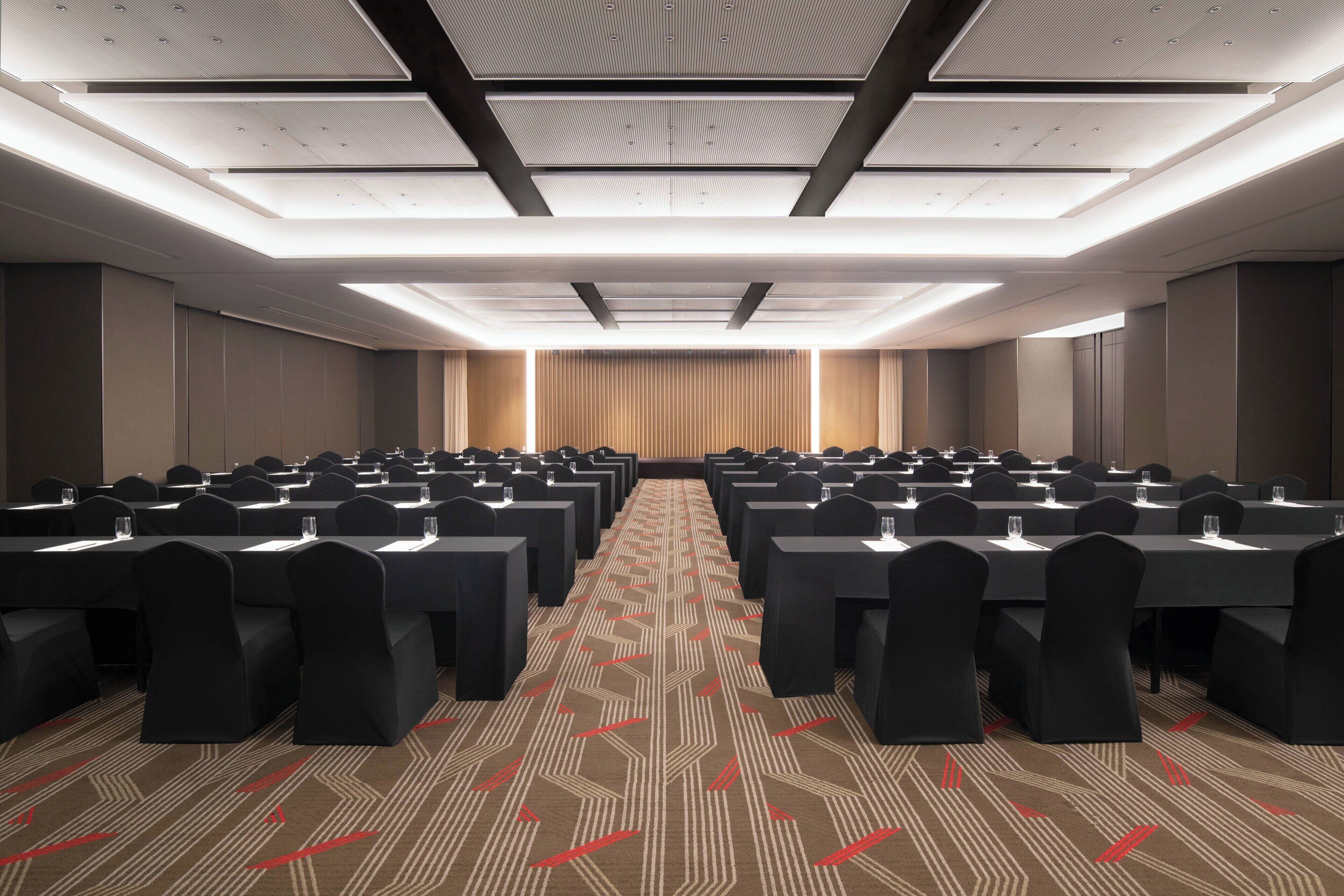 A conference room with multiple tables and chairs, a patterned carpet, and a ceiling with recessed lighting.
