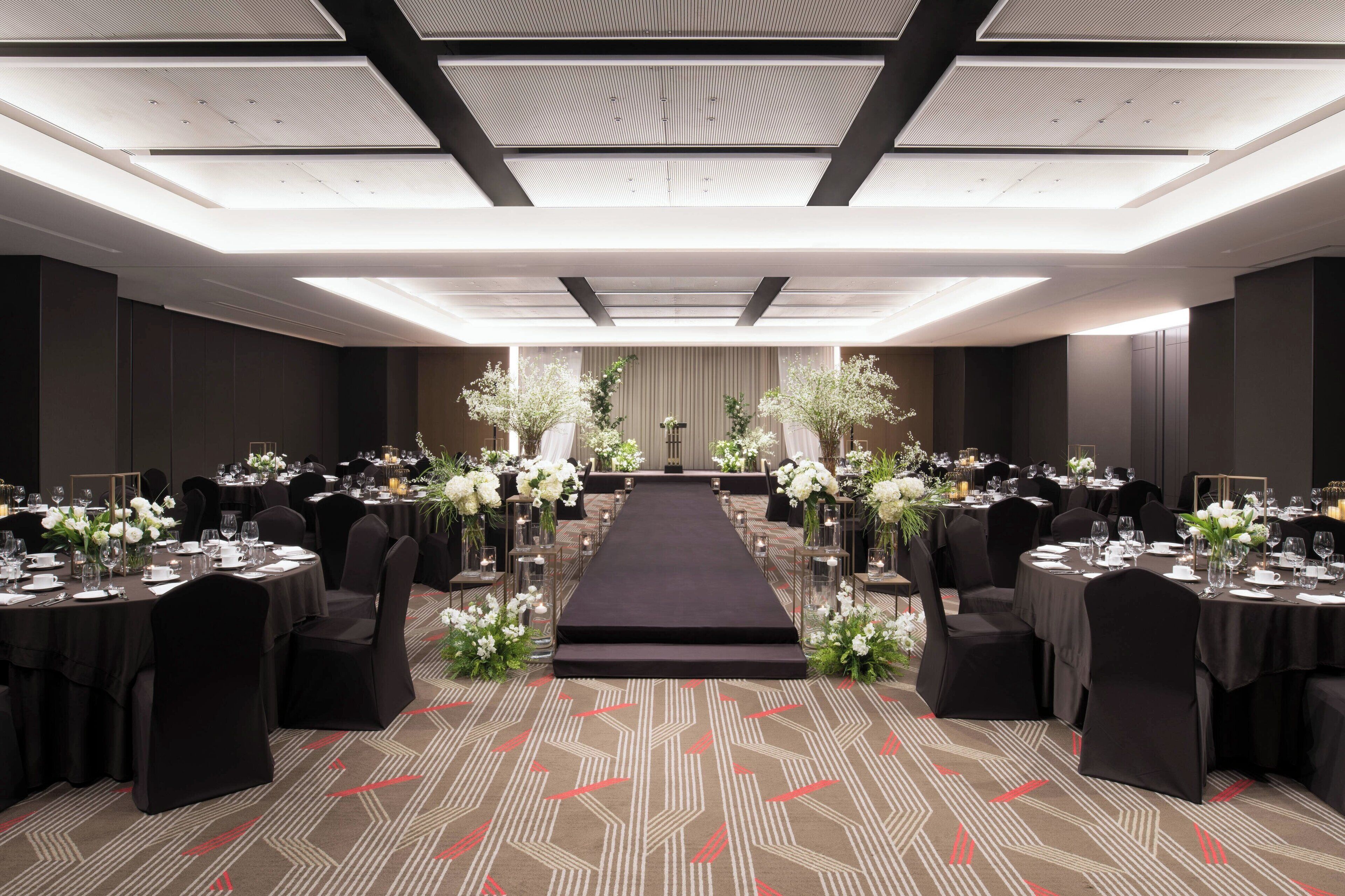 Un salón de banquetes con un pasillo central, mesas dispuestas para comer y arreglos florales.