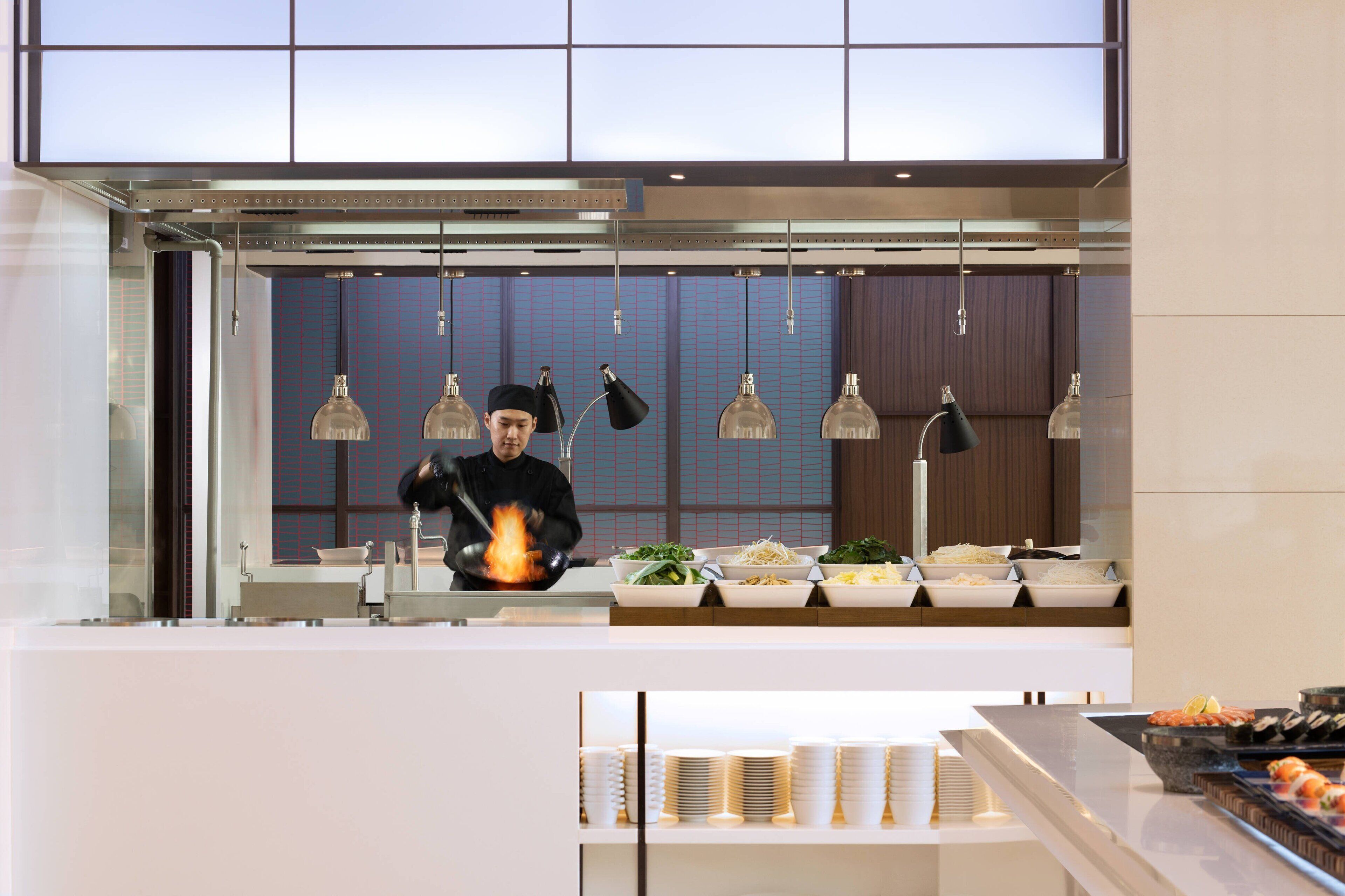 Eine moderne Küche mit Koch, einem Buffet mit verschiedenen Speisen und hängenden Pendelleuchten.