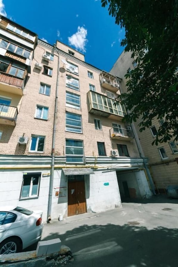 A multi-story residential building with balconies, a garage, and a white car parked in front.