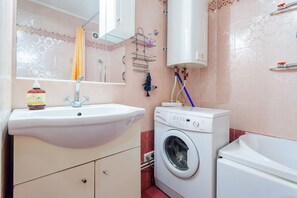 A bathroom with a sink, a washing machine, a mirror, and a shower curtain.