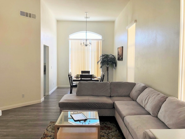 A spacious living room with a large sectional sofa, a glass coffee table, and a dining area in the background.