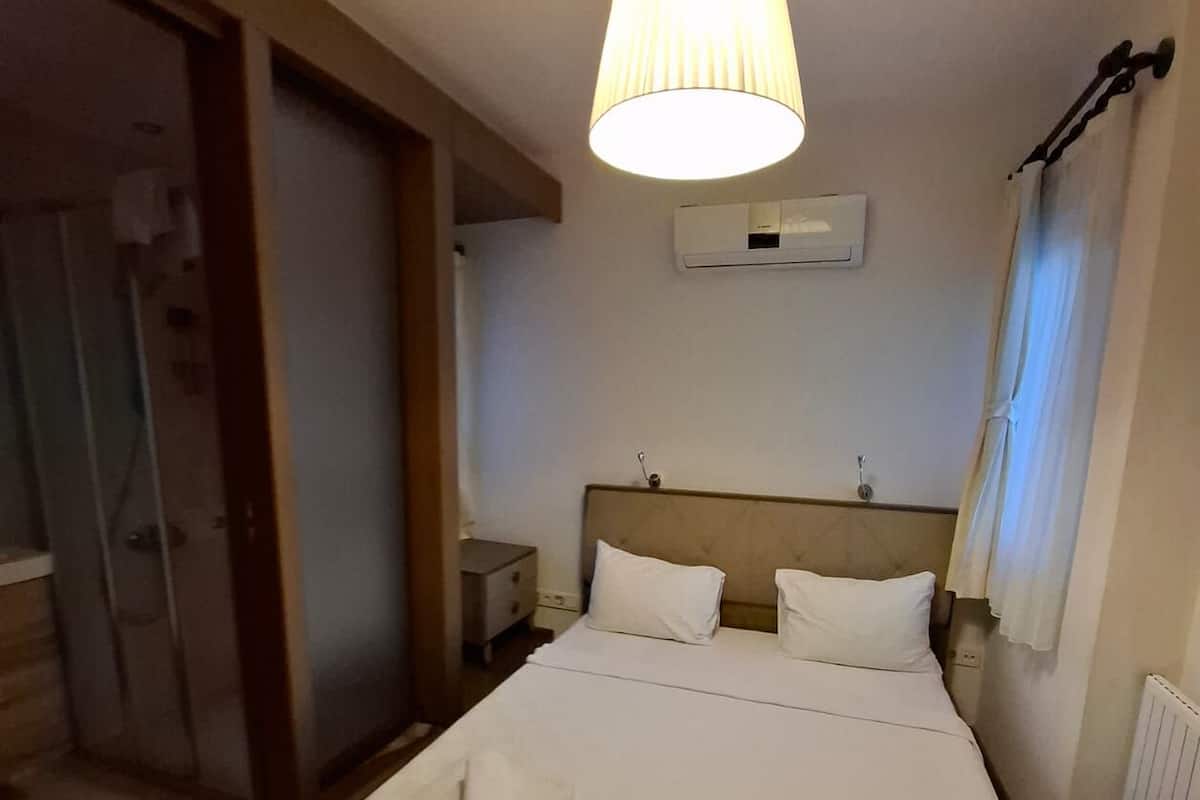 Una habitación de hotel con cama, mesita de noche, unidad de aire acondicionado y lámpara colgante.