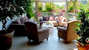 A sunlit patio with a sofa, chairs, and a coffee table, surrounded by potted plants and a view of a garden. - Egehan Butik Otel (Ortaca)