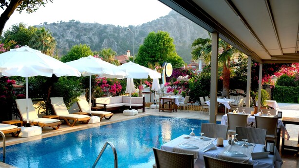 A poolside area with lounge chairs, umbrellas, and dining tables set up for guests. - Egehan Butik Otel (Ortaca)
