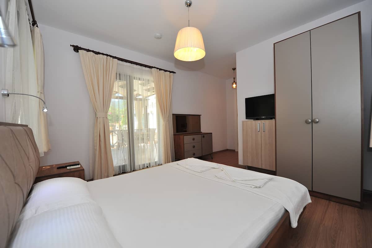 Una habitación de hotel con una cama, televisor, armario y escritorio con lámpara.