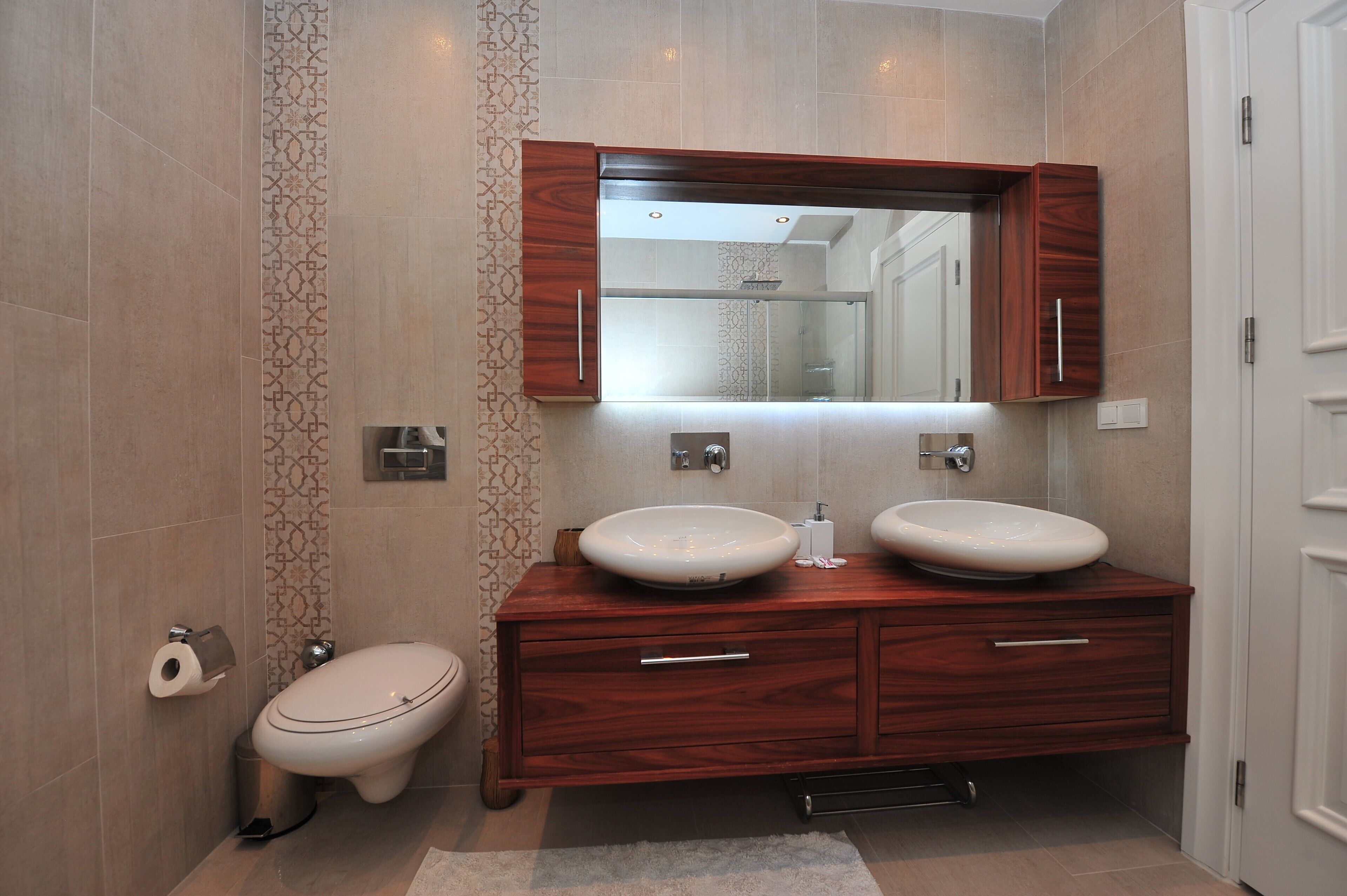 A modern bathroom with two sinks, a toilet, and a large mirror above the vanity.