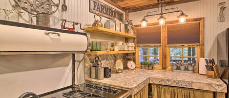 Een rustieke keuken met een boerderijbord, houten planken, een fornuis en een raam met luiken.