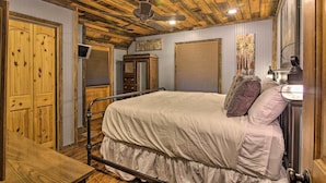 A bedroom with a wooden ceiling, a bed with a white bedspread, a wooden wardrobe, and a wall-mounted TV. - Tubes & Outdoor Games: North Georgia Mtn Retreat (Sautee Nacoochee)