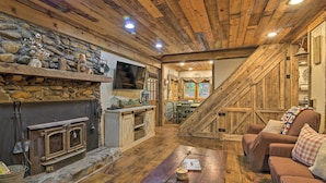 A rustic interior with a stone fireplace, wooden beams, a wooden staircase, and a cozy seating area. - Tubes & Outdoor Games: North Georgia Mtn Retreat (Sautee Nacoochee)