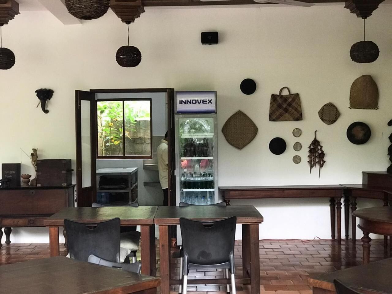 A restaurant interior with wooden tables and chairs, a refrigerator with a beverage dispenser, and various wall decorations.