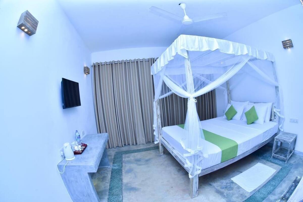 A bedroom with a canopy bed, a flat-screen TV, a bedside table, and a small bedside table with a lamp.