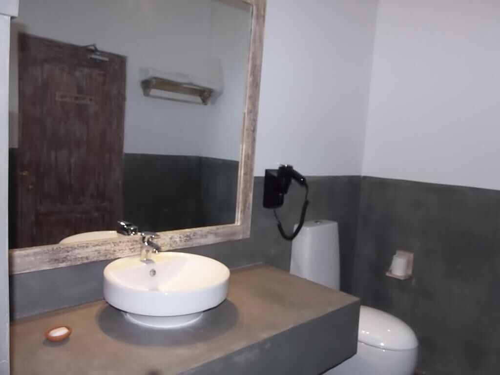 Ein Badezimmer mit rundem Waschbecken, einem Spiegel, einem Handtuchspender und einer Toilette.