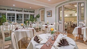 Un restaurant doté de plusieurs tables rondes, de chaises blanches et offrant une vue sur l’extérieur grâce à de grandes fenêtres.
