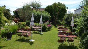 Un espace extérieur aménagé en jardin, avec des tables et des chaises, entouré d’une végétation luxuriante et d’arbres.