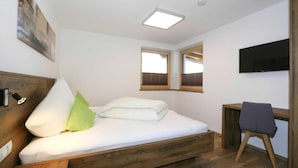 Une chambre avec un lit en bois, un bureau, une chaise et un téléviseur fixé au mur.