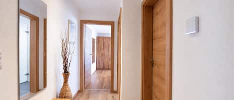 A hallway with wooden flooring, a bench, a vase with branches, and a door.