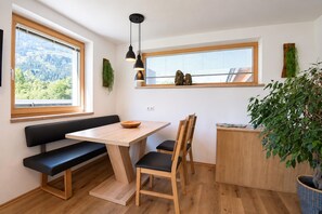 Een moderne keuken met een houten tafel, zwarte stoelen, een bankje en een raam met uitzicht op groen.