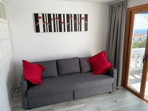 A grey sofa with red cushions, a black and white striped artwork above it, and a view of the outdoors through a glass door. - Los Cristianos Port Royale 157 (Los Cristianos)