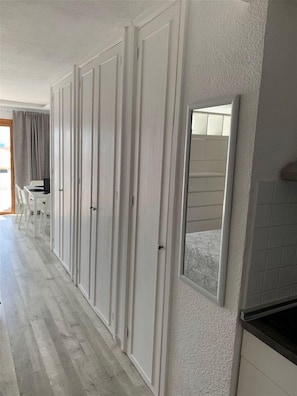 A hallway with a row of white wardrobes, a small seating area with chairs, and a mirror on the wall. - Los Cristianos Port Royale 157 (Los Cristianos)
