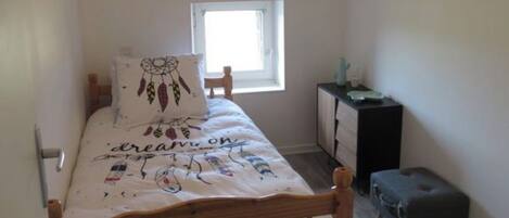 Una habitación pequeña y estrecha con una cama individual, una ventana, un escritorio pequeño y una silla.