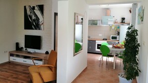 A modern living room with a flat-screen TV, a sofa, and a dining area with green chairs. A potted plant is visible in the corner. - LUCIJA 1 - Enjoy the Rovinj (Rovinj)