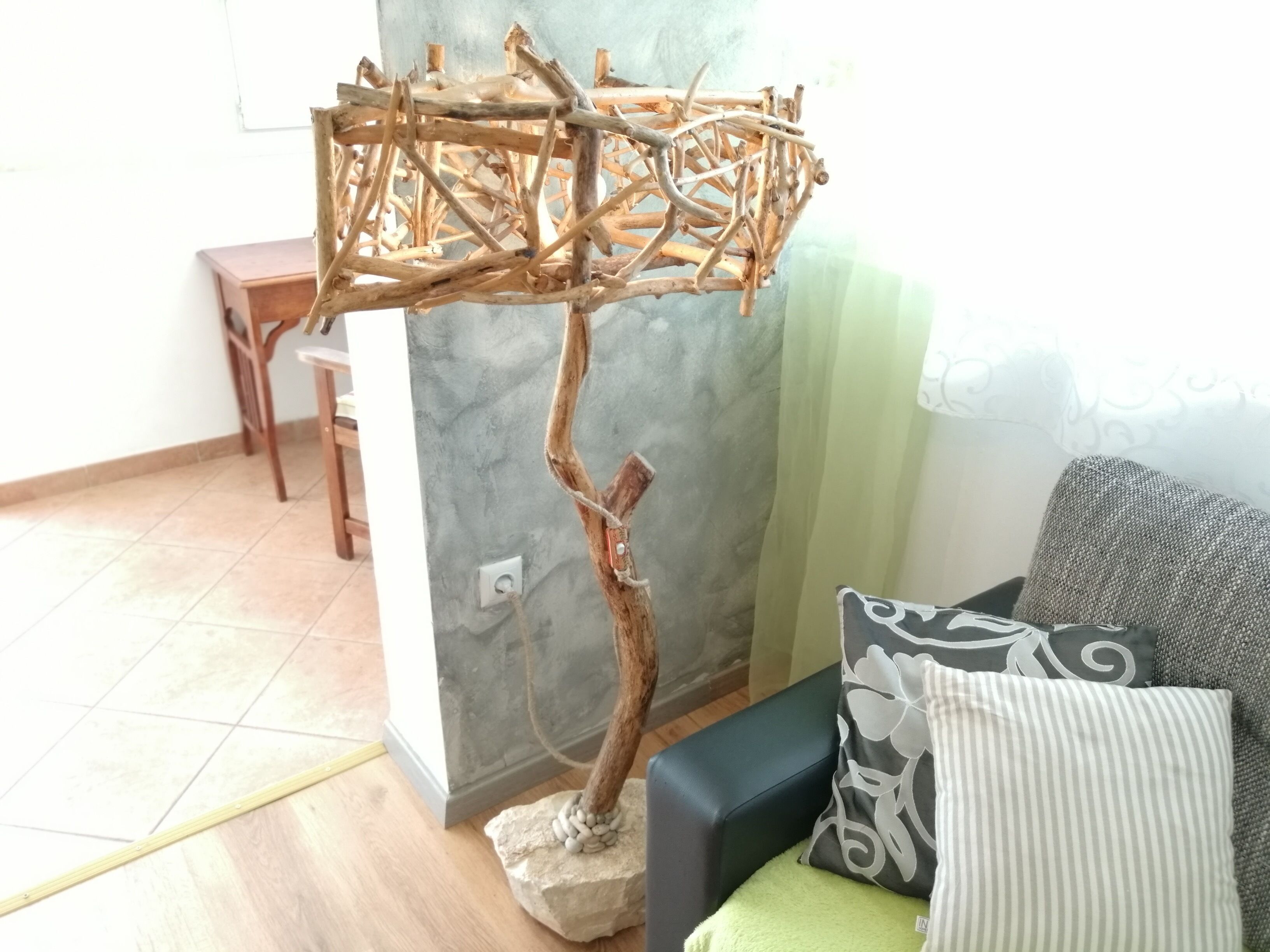 Een kamer met een houten boomsculptuur, een bank met gestreepte kussens en een kleine tafel.