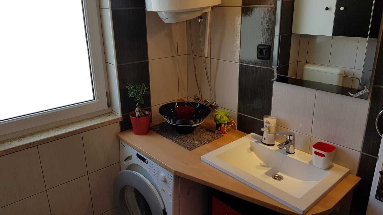 Een kleine badkamer met een wasmachine, een wastafel en een spiegel.