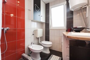 A bathroom with red and white tiles, a white toilet, a bidet, and a window. - Apartment Lucija 2 with unique details (Rovinj)