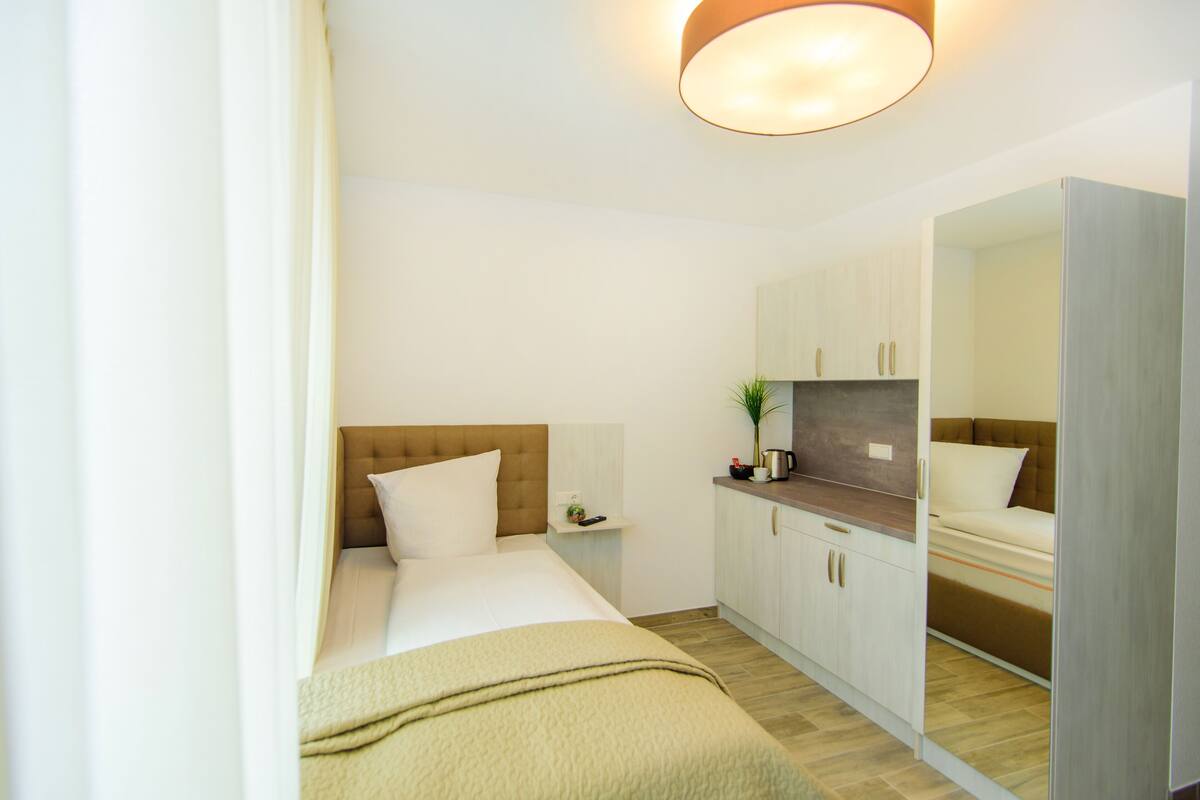 A modern hotel room with a bed, a bedside table, a mirror, and a wardrobe.