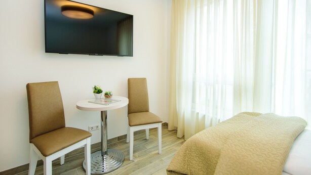 A hotel room with a bed, two chairs, a small table, a TV mounted on the wall, and a window with curtains. - Hotel Filderhof Reutlingen (Reutlingen)