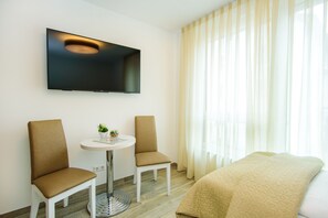 A hotel room with a bed, two chairs, a small table, a TV mounted on the wall, and a window with curtains. - Hotel Filderhof Reutlingen (Reutlingen)