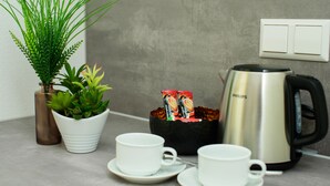 A kitchen counter with a white coffee cup, a white saucer, a black coffee pot, a potted plant, and a container with coffee pods. - Hotel Filderhof Reutlingen (Reutlingen)