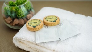 A neatly folded white towel, two round soap bars, and a small glass bowl with green plants and brown pebbles. - Hotel Filderhof Reutlingen (Reutlingen)