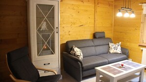 A wooden interior with a grey sofa, a cabinet with glass doors, and a table with a red object. - Where nature lives ... enjoy your vacation. (Drognitz)