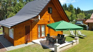 A wooden cabin with a tiled roof, a patio with a table and chairs, and a green umbrella. - Where nature lives ... enjoy your vacation. (Drognitz)