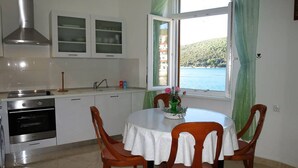 Una cucina con piano cottura, forno e pensili, un tavolo da pranzo con sedie, e una finestra che si affaccia su uno specchio d'acqua e del verde.