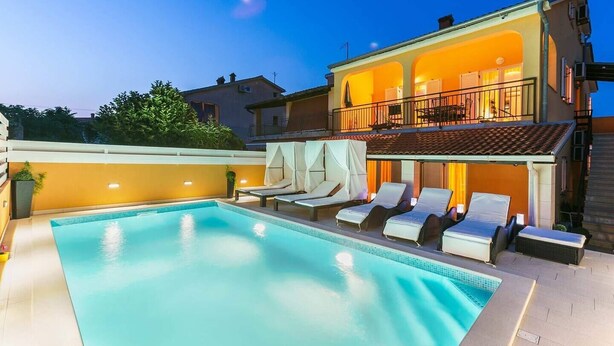 A swimming pool with lounge chairs and a covered seating area, surrounded by a building with a balcony. - Holiday house Vesna for relaxed vacation (Medulin)