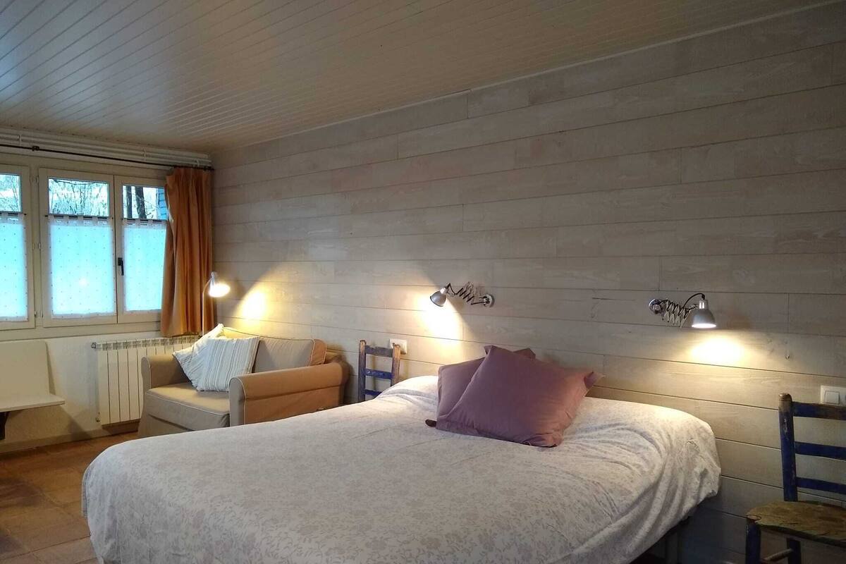 Un dormitorio con una cama, dos mesitas de noche, una silla y dos lámparas de pared.