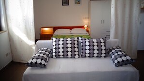 A neatly made bed with a patterned bedspread and two pillows, a bedside table with a lamp, and a wall-mounted light fixture. - Nice Studio apartments Eduard (Medulin)