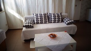 A living room with a sofa, patterned cushions, a small table with a bowl, and a curtain with a pin pattern. - Nice Studio apartments Eduard (Medulin)