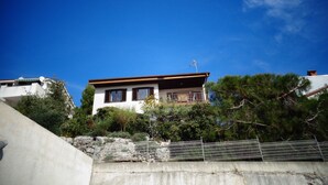A two-story house with a balcony, surrounded by trees and a stone wall. - Nice Studio apartments Eduard (Medulin)
