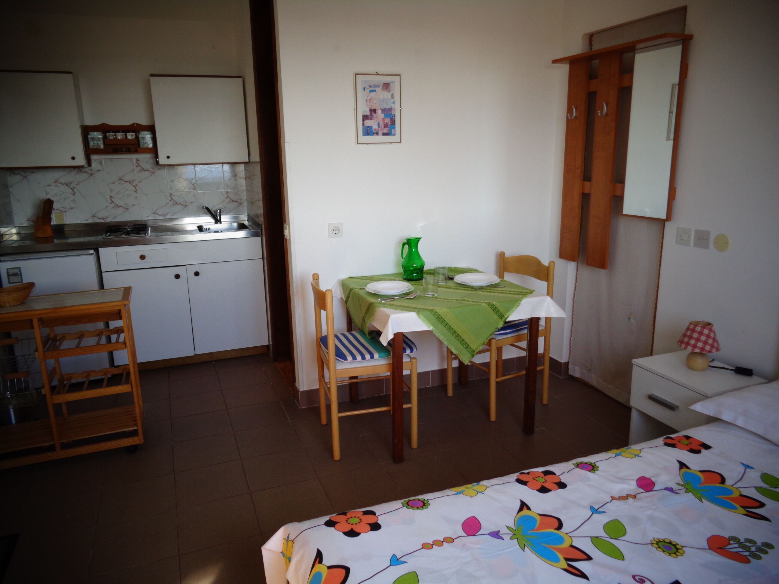 Une cuisine compacte avec un coin repas, un lit recouvert d’une couvre-lit à motifs floraux et une petite table de chevet avec une lampe.