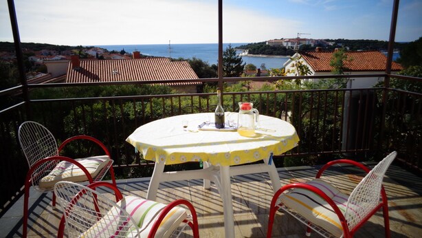 A balcony with a table and chairs, overlooking a coastal view with buildings and a clear sky. - Nice Studio apartments Eduard (Medulin)
