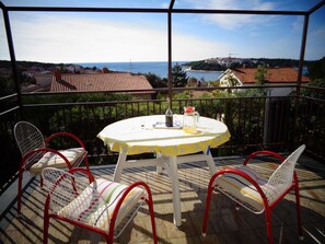 A balcony with a table and chairs, overlooking a coastal view with buildings and a clear sky. - Nice Studio apartments Eduard (Medulin)