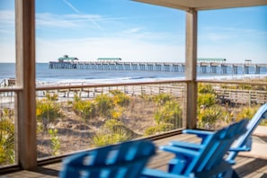 A beach view from inside a building with a wooden deck and blue chairs. - 211 E Arctic Ave - Tee "Fore" Two - Oceanfront Beach House with Private Beach Access! (Folly Beach)