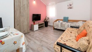Huone, jossa on ruokapöytä valmiina, sohva, sänky, televisio ja puinen vaatekaappi.